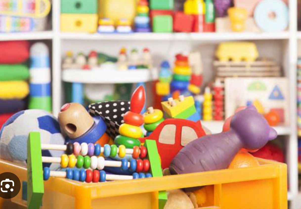 **Alt text (in Italian):**  
Colorati giocattoli per bambini in plastica e legno in una scatola gialla.